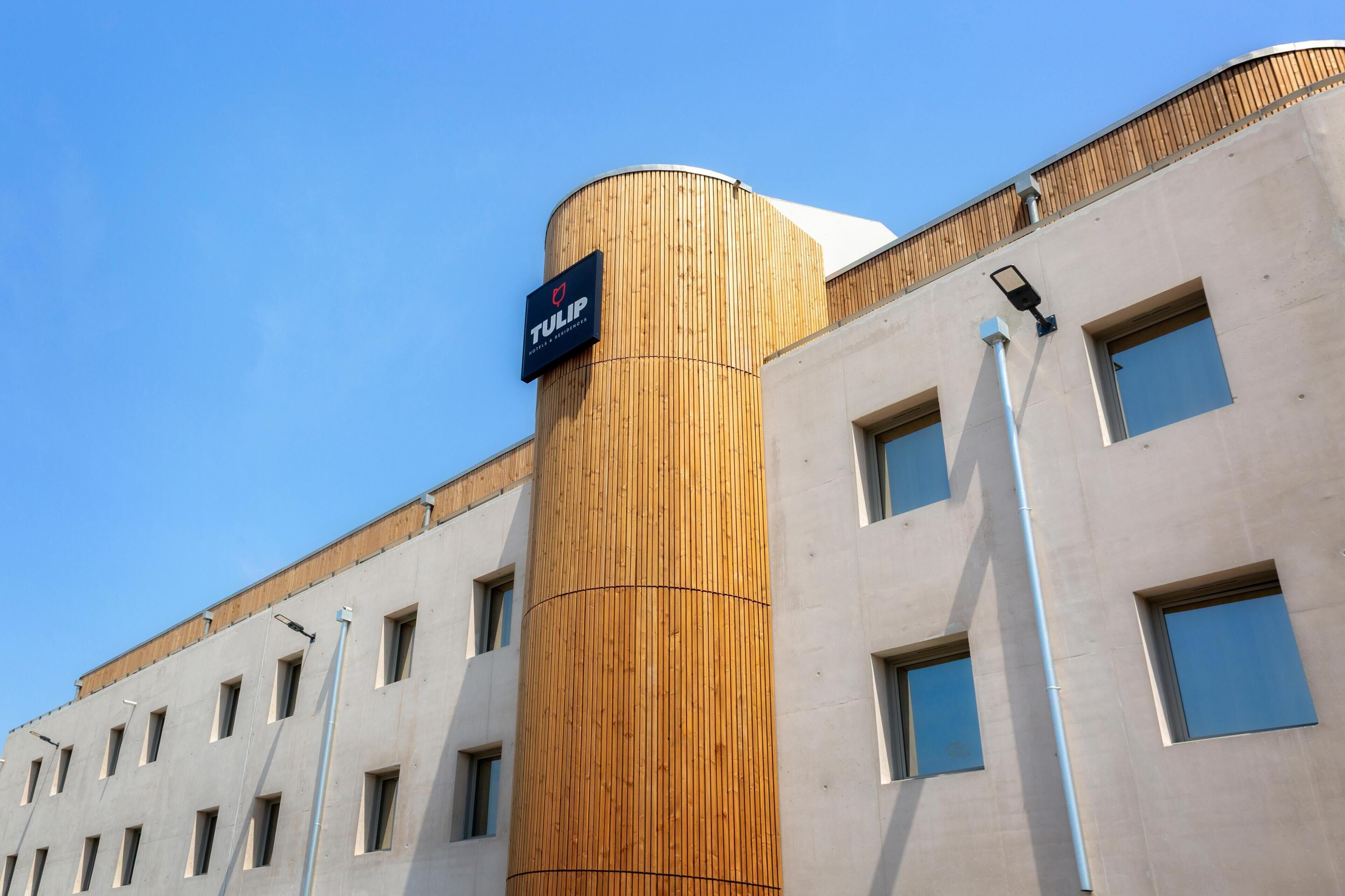 Een modern hotel met een cilindervormige houten gevel en een bord waarop staat dat het een hotel en residentie is.
