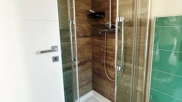 A glass-enclosed shower with a handheld showerhead and a wall-mounted faucet.