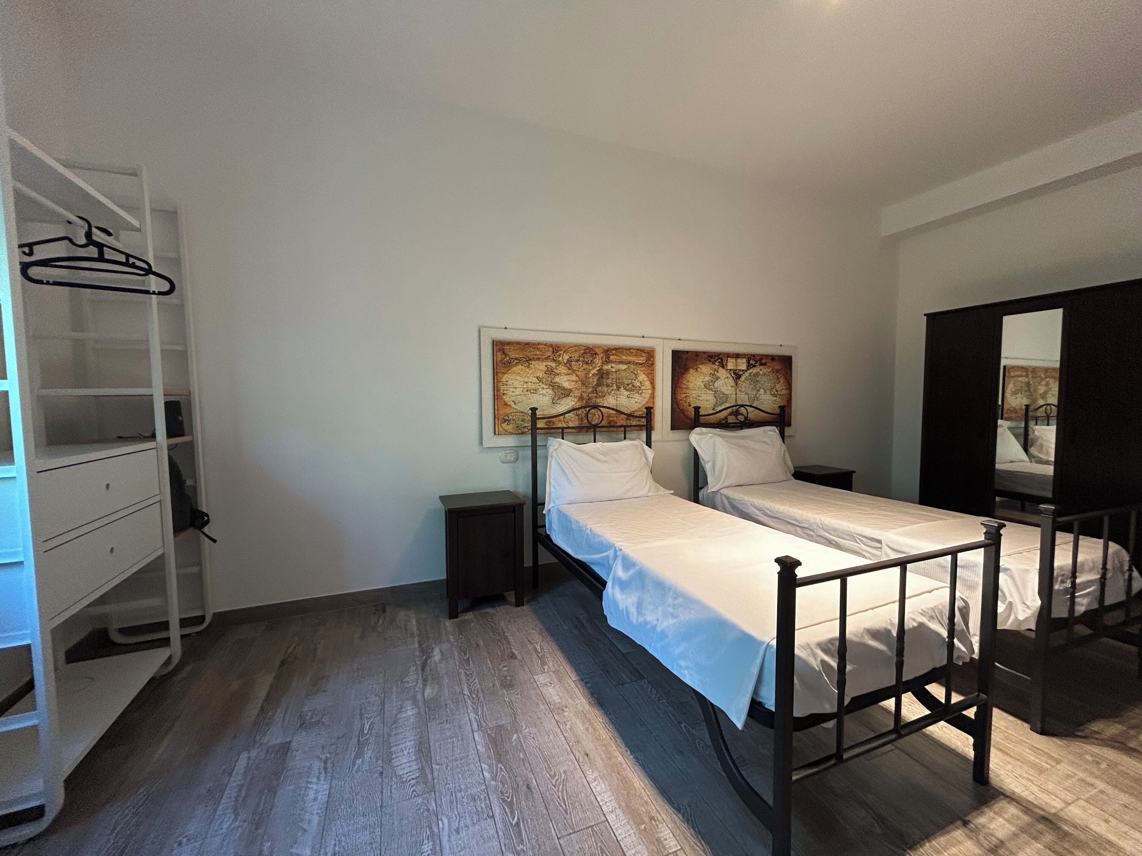 Een slaapkamer met twee eenpersoonsbedden, een kledingkast, een klein nachtkastje en een spiegel.