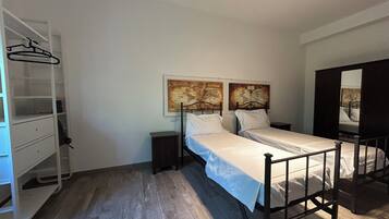 Een slaapkamer met twee eenpersoonsbedden, een kledingkast, een klein nachtkastje en een spiegel.