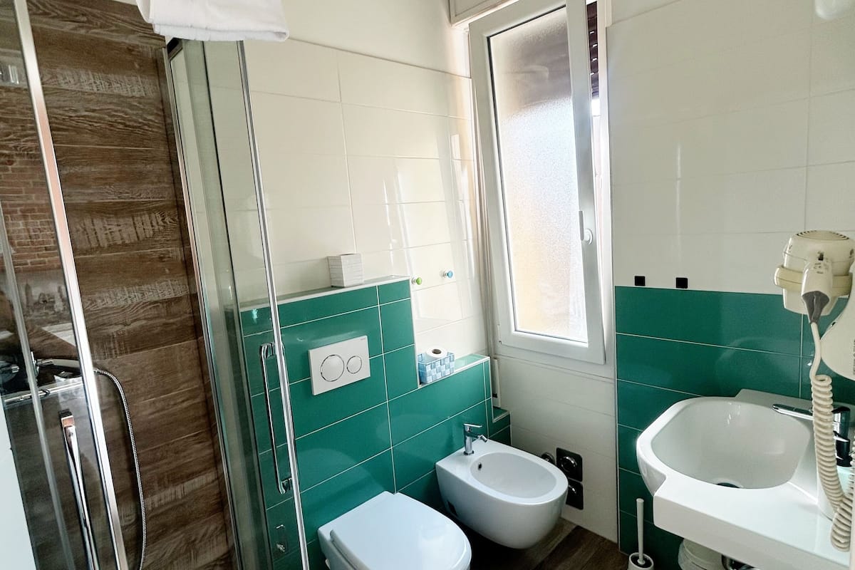 Un baño moderno con cabina de ducha de vidrio, un bidé, un lavabo y una ventana que proporciona luz natural.