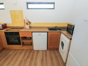 A compact kitchen with a dishwasher, washing machine, microwave, and a small window above the sink. - Brookview Goldfinch (Haverfordwest)