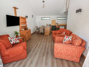 Ein kompakter Wohnbereich mit Sofa, Holzschrank, Flachbildfernseher, Esstisch und Küchenzeile.