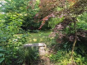 Ein Garten mit einer Steinsitzbank, dichtem Grün und einem kleinen Teich.