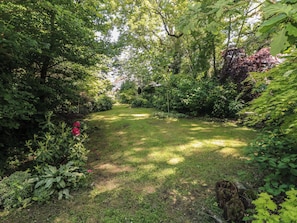 Ein üppiger Garten mit verschiedenen Pflanzen und Bäumen, einem ebenen Weg und einer Holzkonstruktion.