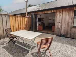 Un patio con una mesa y sillas, una cerca de madera y un edificio con una puerta abierta que da a un espacio interior.