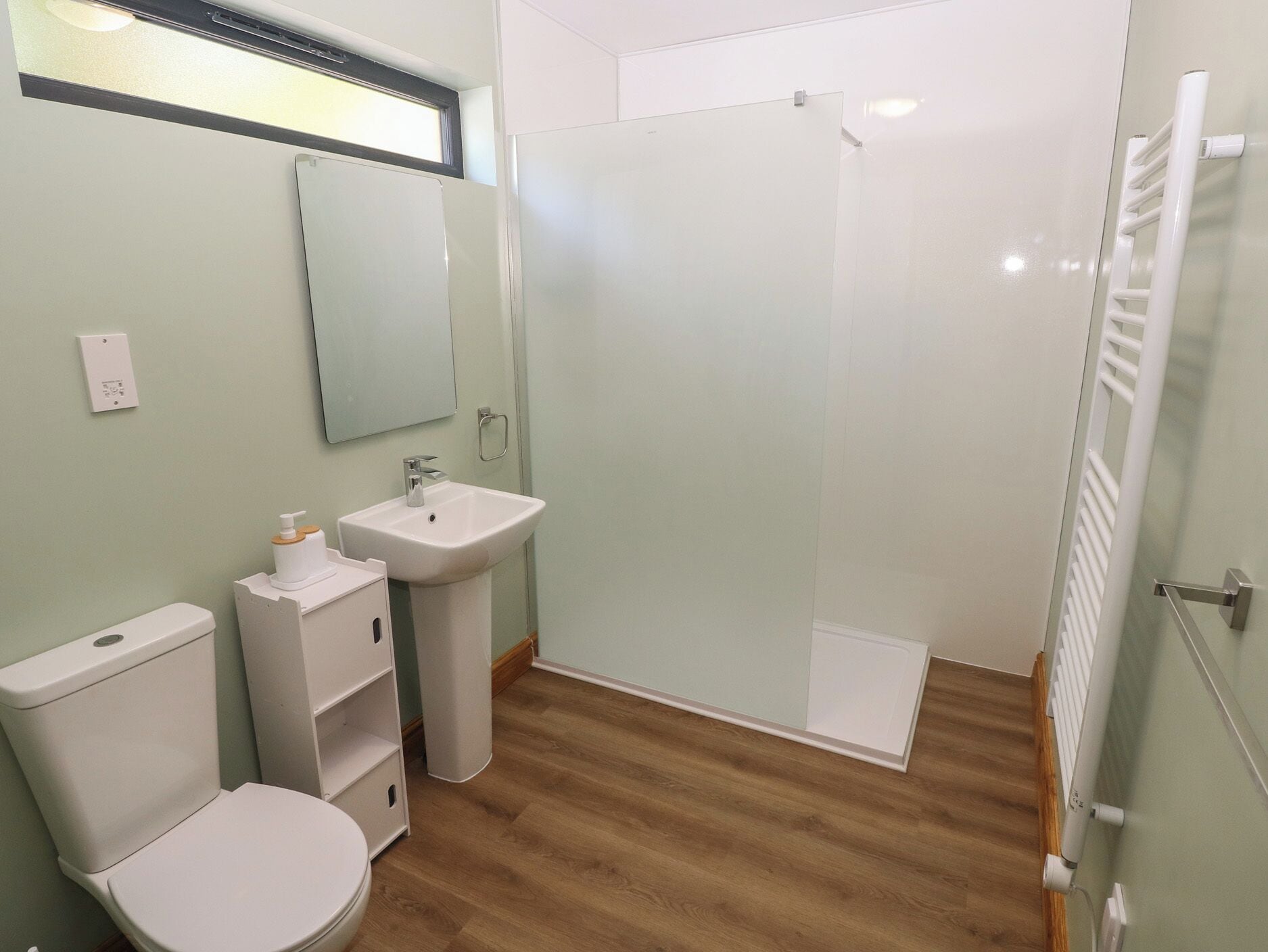 A bathroom with a toilet, sink, mirror, and glass shower enclosure.