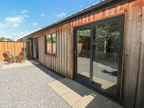 A wooden building with a patio, a sliding glass door, and a table with chairs. - Brookview Goldfinch (Haverfordwest)
