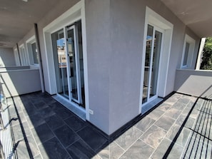 Un balcón con puertas de cristal, piso de baldosas y barandilla.