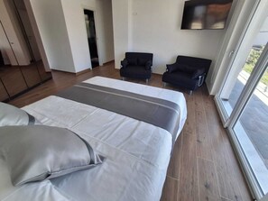 Una habitación de hotel moderna con una cama grande, dos sillones, televisor y vistas al balcón.