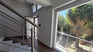 Un intérieur moderne avec un escalier, une grande fenêtre donnant sur un espace verdoyant et une porte menant à une autre pièce.