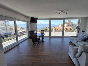 Un'ampia zona giorno con tavolo da pranzo, divano e grandi finestre che si affacciano sulla città e sul mare.