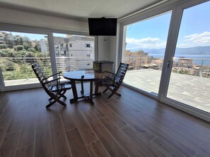 Un balcón con mesa y sillas, un televisor montado en la pared y vistas al mar y a edificios.