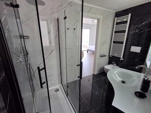Un bagno moderno con doccia vetrata, lavabo bianco e pavimento in marmo nero.
