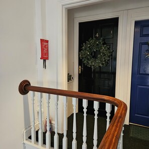 A staircase with white balusters and a wooden handrail, leading to a black door with a wreath. - Park View Penthouse Suite (Southport)