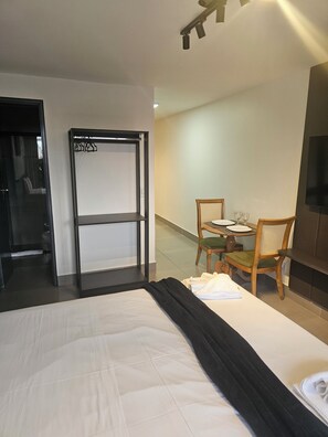 Et hotelværelse med en seng, et bord med stole, et fjernsyn og en dør til et andet rum.