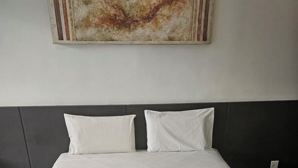 A neatly made bed with white linens, a dark headboard, and a single white pillow. - Flat 109 Norte Novo e Completo 206 (Brasília)