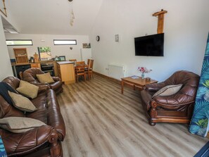 A living room with a brown leather sofa, a wooden coffee table, and a television mounted on the wall. - Brookview Kingfisher (Haverfordwest)