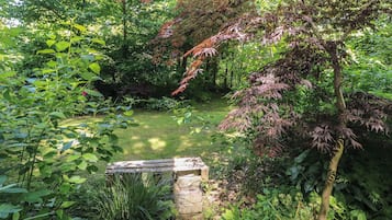 Un jardín con un banco de piedra, follaje denso y un pequeño estanque.