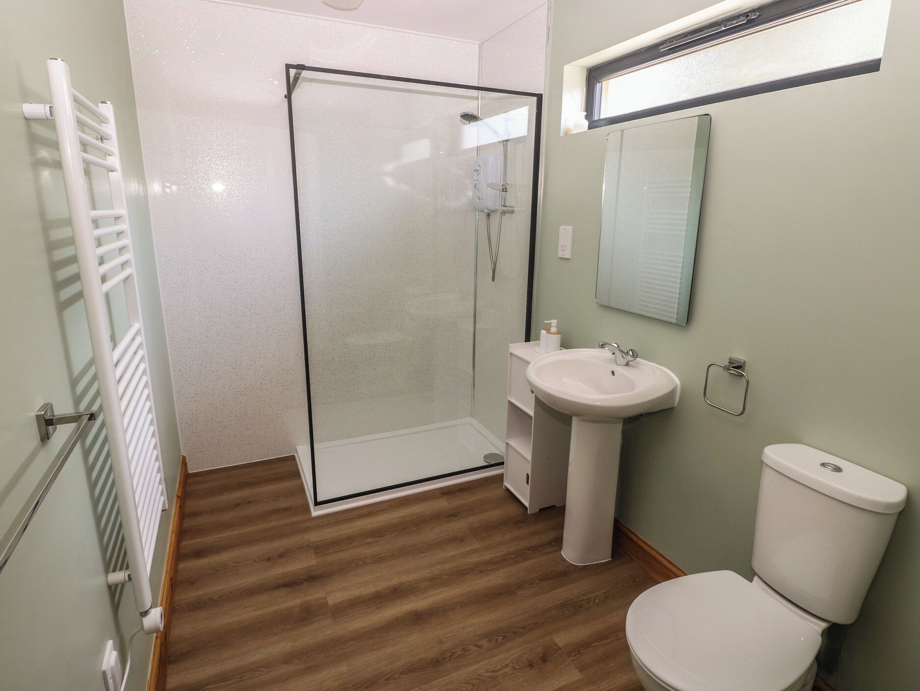 A bathroom with a glass shower enclosure, a pedestal sink, a toilet, and a towel rack.