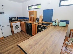 A compact kitchen with a microwave, washing machine, dishwasher, and a wooden countertop. - Brookview Kingfisher (Haverfordwest)