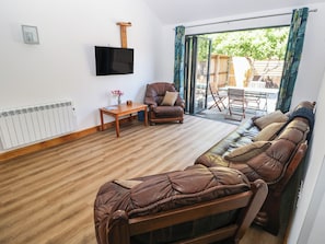 A living room with a sofa, a television mounted on the wall, a table with a vase, and a view through a glass door. - Brookview Kingfisher (Haverfordwest)