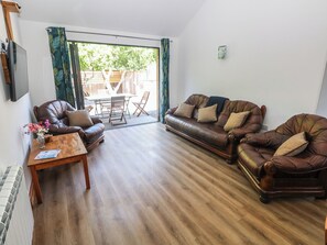 A living room with a brown leather sofa, a wooden coffee table, and a dining area with a table and chairs. - Brookview Kingfisher (Haverfordwest)