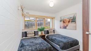 A small, cozy room with two beds, a window with a view, a plant on the windowsill, and a painting of a cow on the wall.