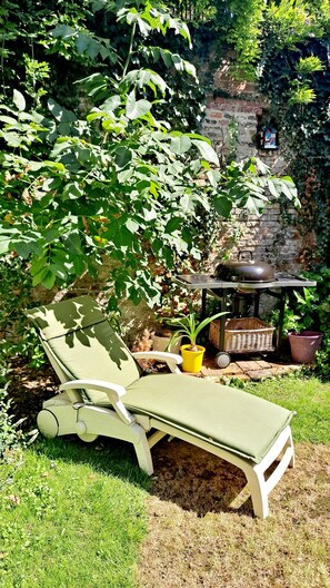 Een tuin met een lounge stoel, een kleine tafel met een waterkoker, en een bakstenen muur op de achtergrond.