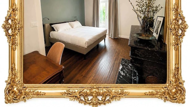 Een slaapkamer met een bed, een bureau, een dressoir en een spiegel met gouden lijst.