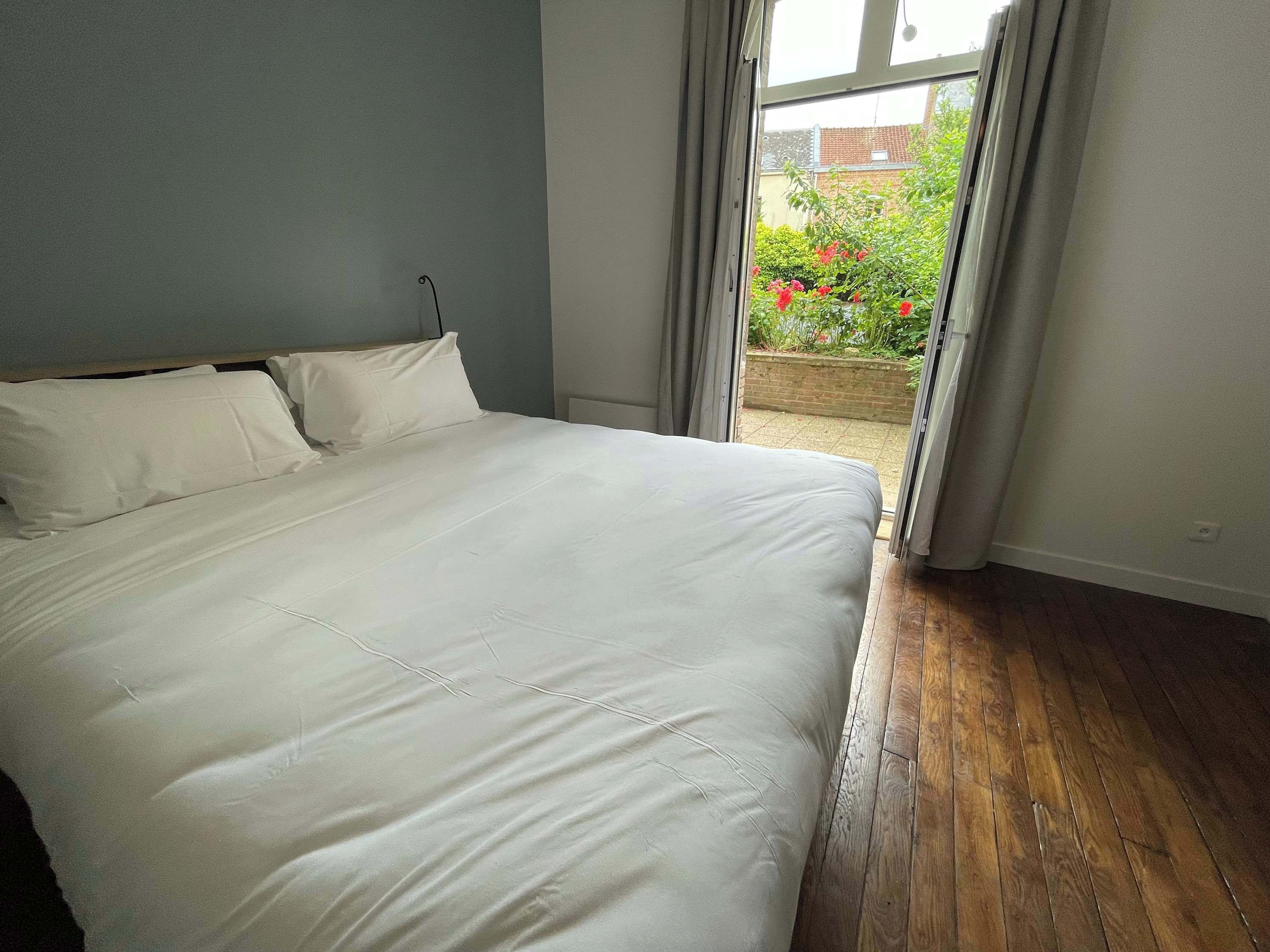 Un dormitorio con una cama grande, una ventana con cortinas y vistas a un jardín.