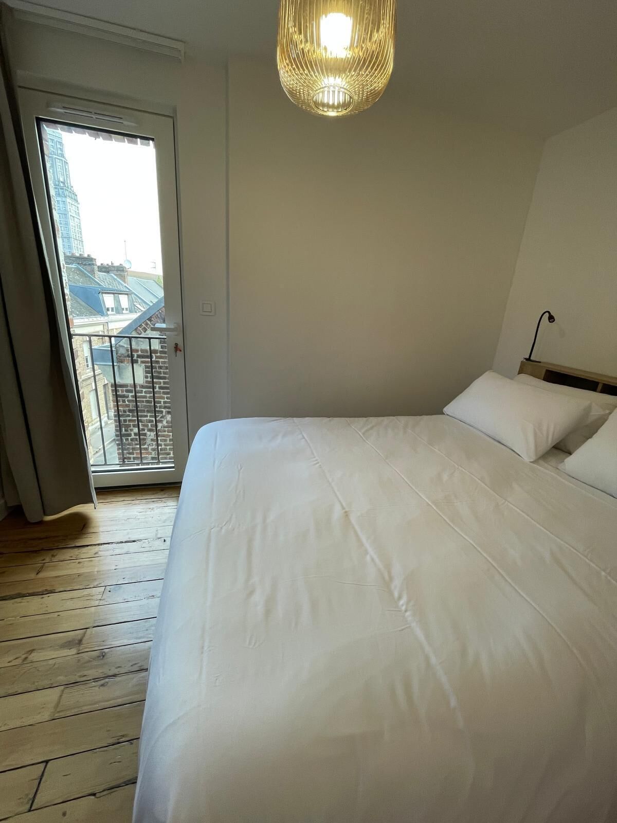 A bedroom with a large bed, a hanging light fixture, and a view through a door.