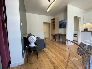 A living room with a grey sofa, a white fan, a wooden coffee table, and a dining area with a wooden table and chairs.