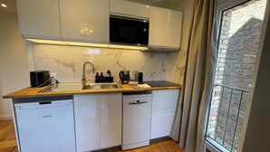 Cozinha moderna com armários brancos, micro-ondas embutido e janela com vista para um prédio de tijolos.