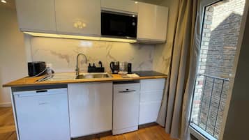 Une cuisine moderne avec des meubles blancs, un four à micro-ondes encastré et une fenêtre donnant sur un immeuble en briques.