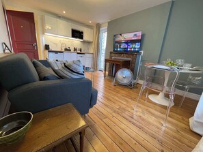 Ein modernes Wohnzimmer mit einer Couch, einem Esstisch mit Stühlen, einer Küchenzeile und einem an der Wand befestigten Fernseher.