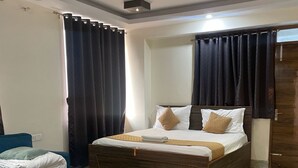 A modern hotel room with a large bed, a blue sofa, a small table, and a wooden door. - Spacious 9-bedroom hotel in charming Patna with AC comfort (Patna)