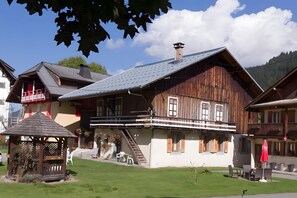 A traditional wooden house with a balcony, a small wooden structure, and a staircase leading to the upper floor.