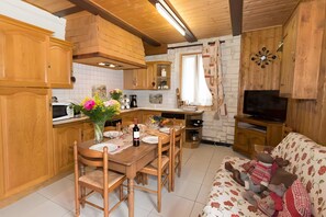 A wooden interior with a dining table set for four, a sofa with stuffed animals, and a television in a wooden cabinet.