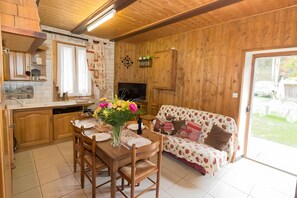 A wooden interior with a dining table set for two, a sofa, and a television.