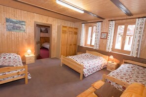 A wooden room with two beds, a wardrobe, and a window with curtains.
