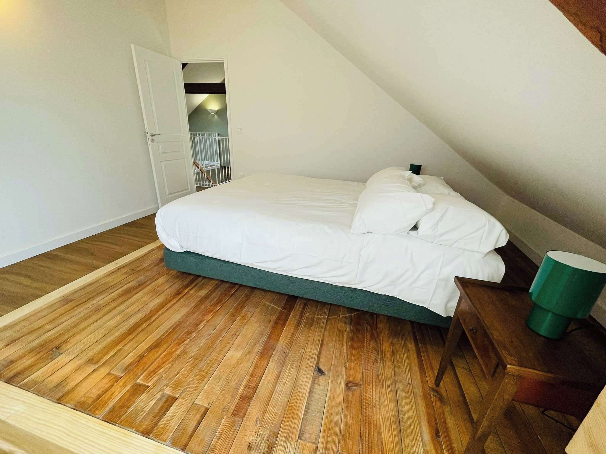 A bedroom with a wooden floor, a bed with white bedding, a green bedside table, and a green trash bin.