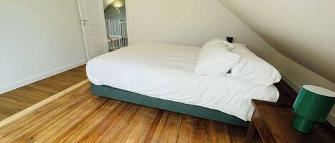 A bedroom with a wooden floor, a bed with white bedding, a green bedside table, and a green trash bin.