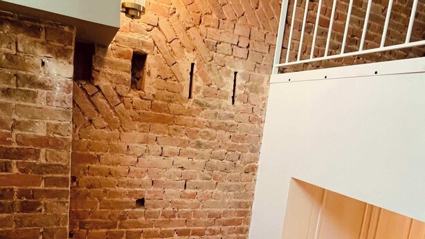 A staircase with a wooden handrail leading to a brick wall with a light fixture. - Spacious Duplex • 2 Suites • Space & Privacy • Fully Equipped • Amiens Centre • 5-min Walk to Station • Parking on Site (Amiens)