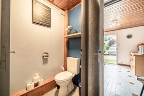 Une salle de bain avec des toilettes, du papier toilette et une étagère ornée de fleurs.