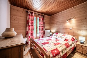 Une chambre dans un chalet en bois, avec un lit, une table de chevet, une lampe et un vase posé sur une table.