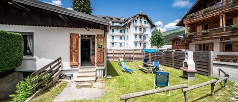 A traditional chalet with a wooden exterior, a small patio with outdoor seating, and a view of the surrounding mountainous landscape.