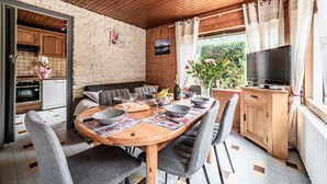 Zona pranzo con tavolo in legno, sedie grigie e televisore su un mobile in legno.