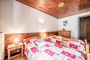 A bedroom with two wooden beds, a nightstand with a lamp, a wooden dresser, and a wooden ceiling.