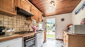 Una cucina con pensili e basi in legno, zoccolo rivestito in piastrelle, piano cottura a gas, lavastoviglie e forno a microonde.